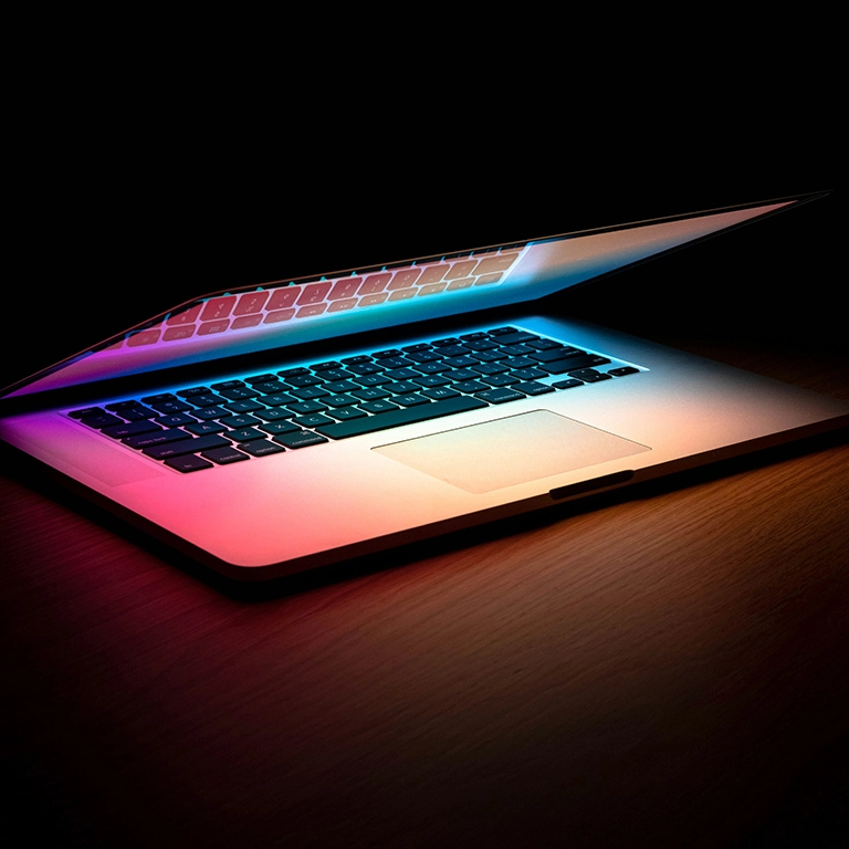 An illuminated MacBook sitting partially open in the dark