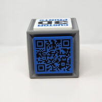 3D printed cube with one side featuring a QR code and the other featuring logos and slogans.