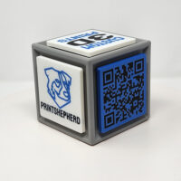 3D printed cube with one side featuring a QR code and the other featuring logos and slogans.