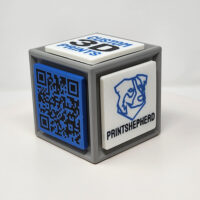 3D printed cube with one side featuring a QR code and the other featuring logos and slogans.